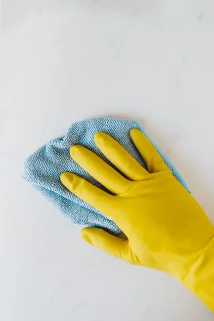 a-woman-in-a-green-shirt-and-black-gloves-vacuuming-a-gray-ottoman-5txz228u4eo